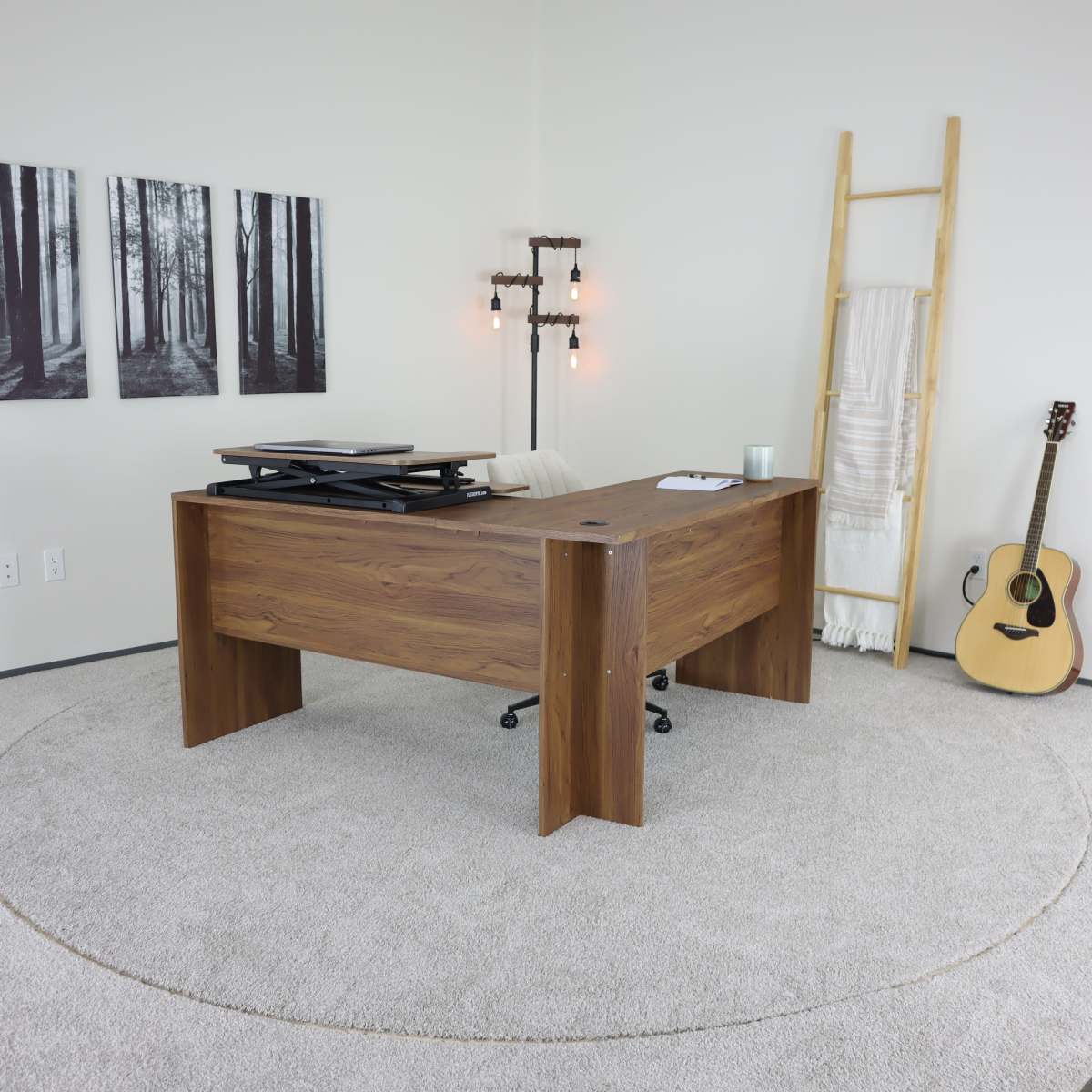 A modern office space features a wooden desk with a rolling chair, surrounded by framed forest photographs and a guitar leaning against a ladder.