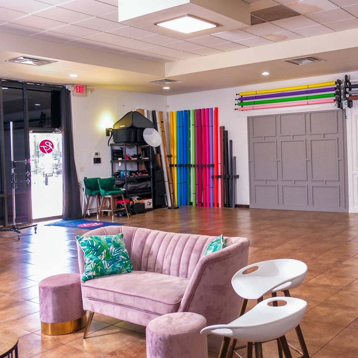 A photography studio featuring a pink couch, two white chairs, and colorful backdrops arranged against the wall.