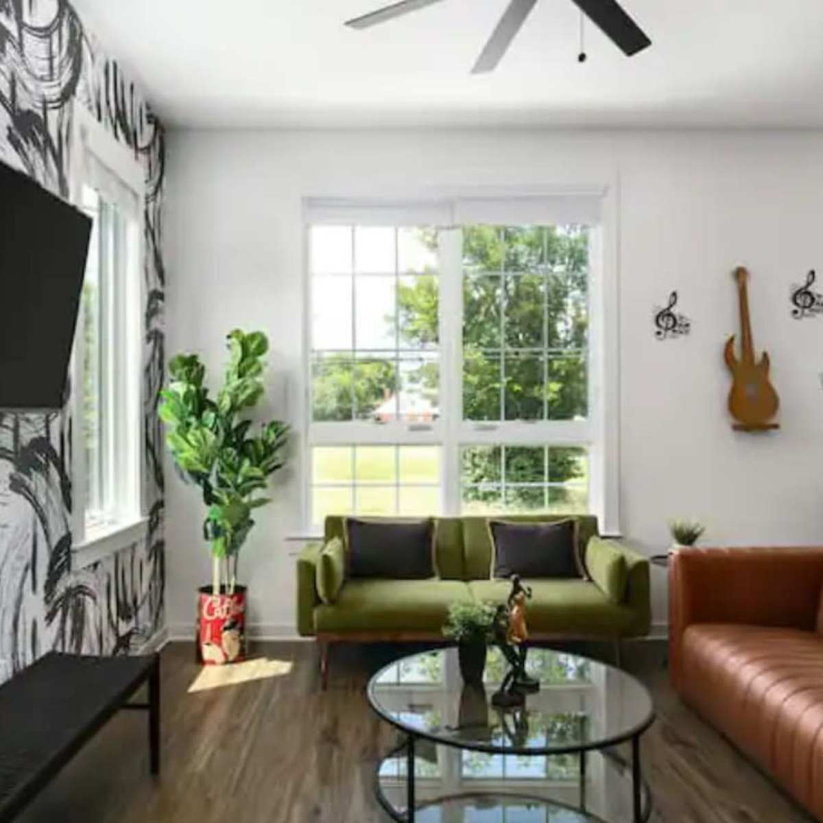 The room features a mix of modern and vintage furniture, including a brown leather sofa, a green couch, and a wall-mounted TV, all set against a decorative black and white wallpaper.