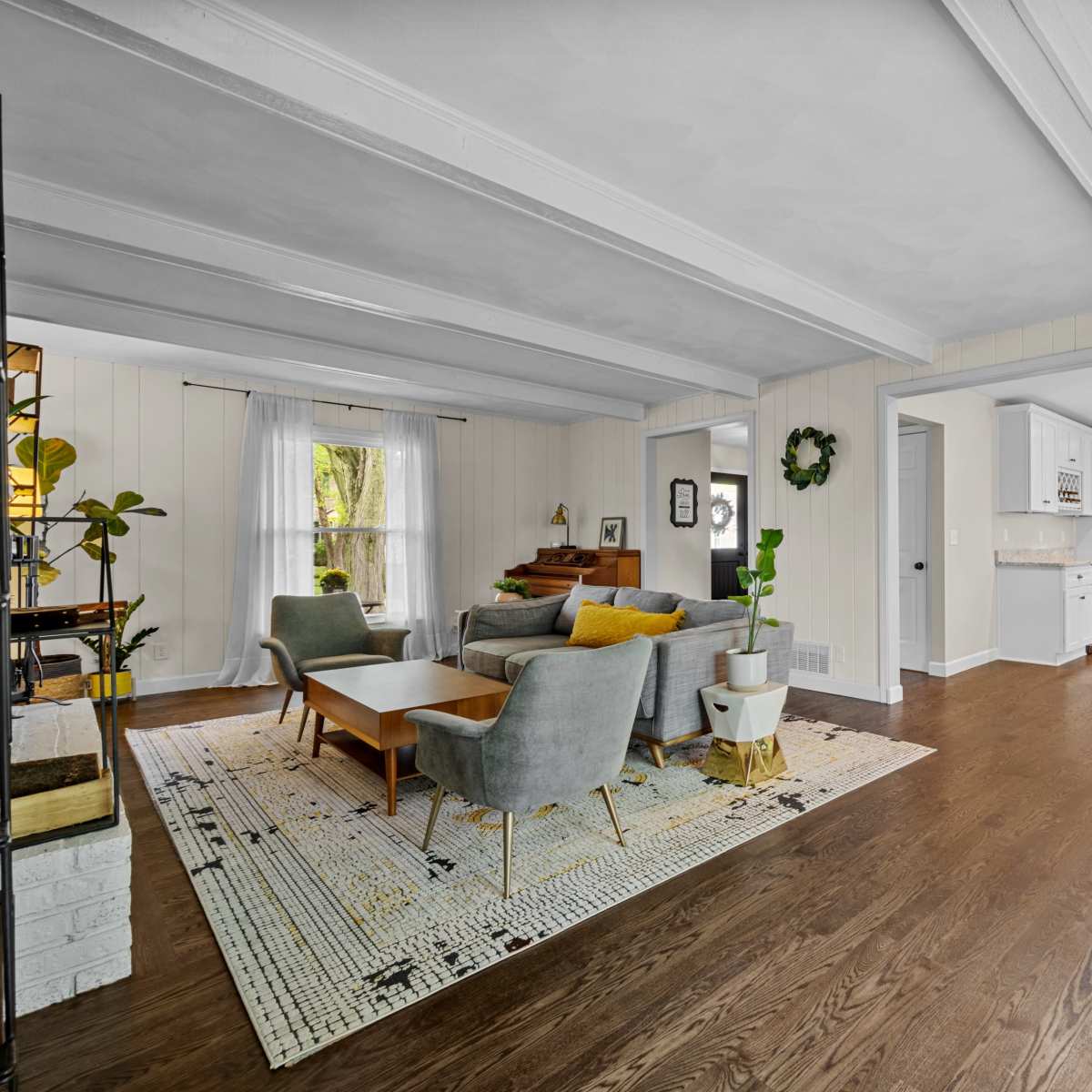A modern living room with gray and wooden furniture, separated from a kitchen area by an archway.