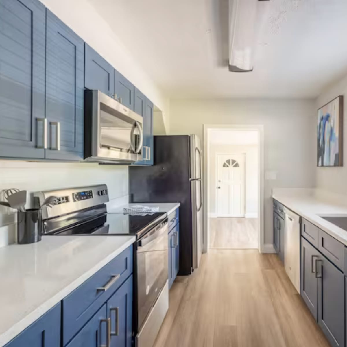 A modern kitchen featuring blue cabinets, stainless steel appliances, and a light-colored countertop with a view toward a door at the end of the room.