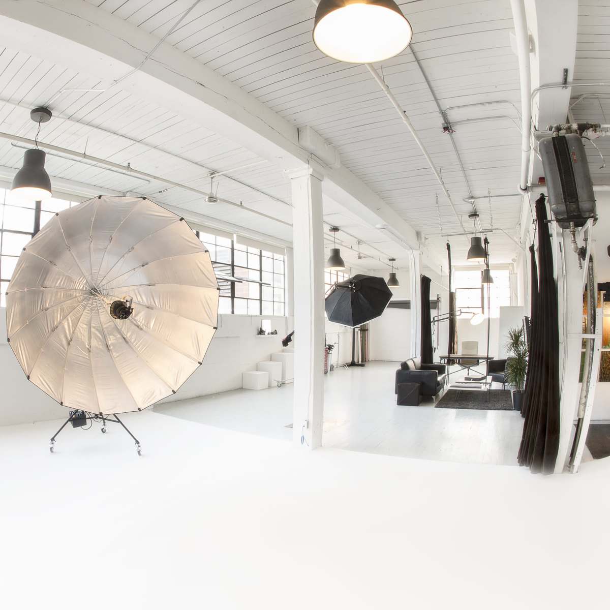 A spacious photography studio featuring large lighting equipment, white walls, and large windows.