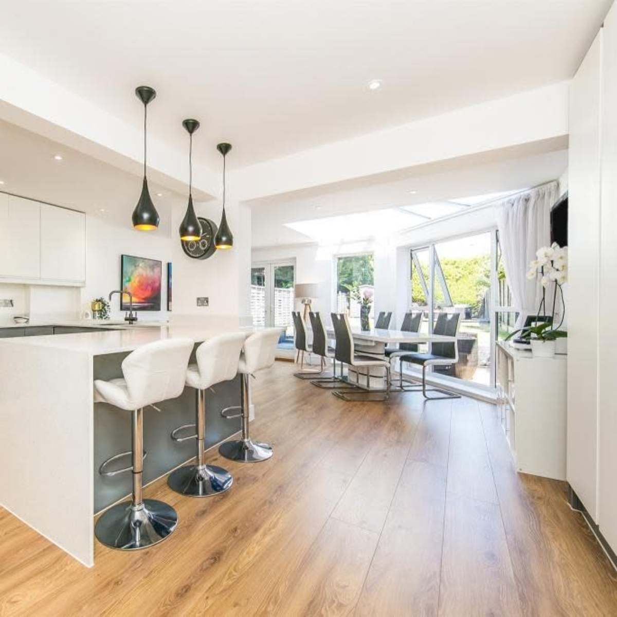 A modern kitchen with a large island, sleek cabinetry, and a dining area featuring a table surrounded by chairs, illuminated by pendant lights.