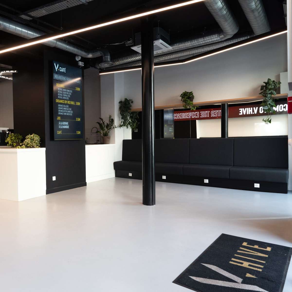 A modern reception area with a white counter, black seating along the walls, and a large screen displaying information.