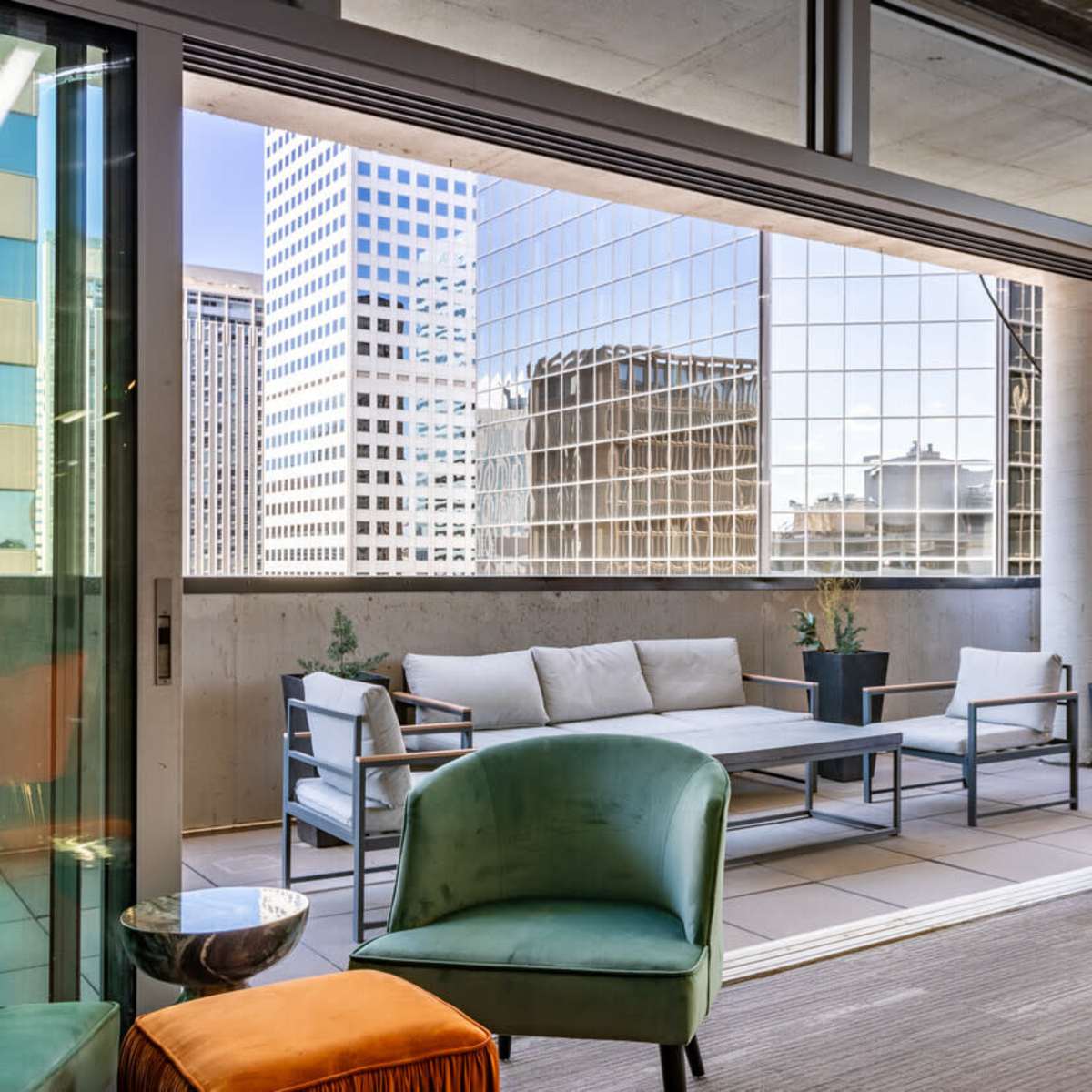 A modern indoor space opens to a balcony with outdoor seating and views of surrounding skyscrapers.