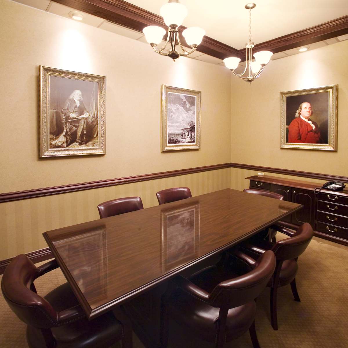 A conference room features a long wooden table surrounded by leather chairs, with framed portraits on the walls.