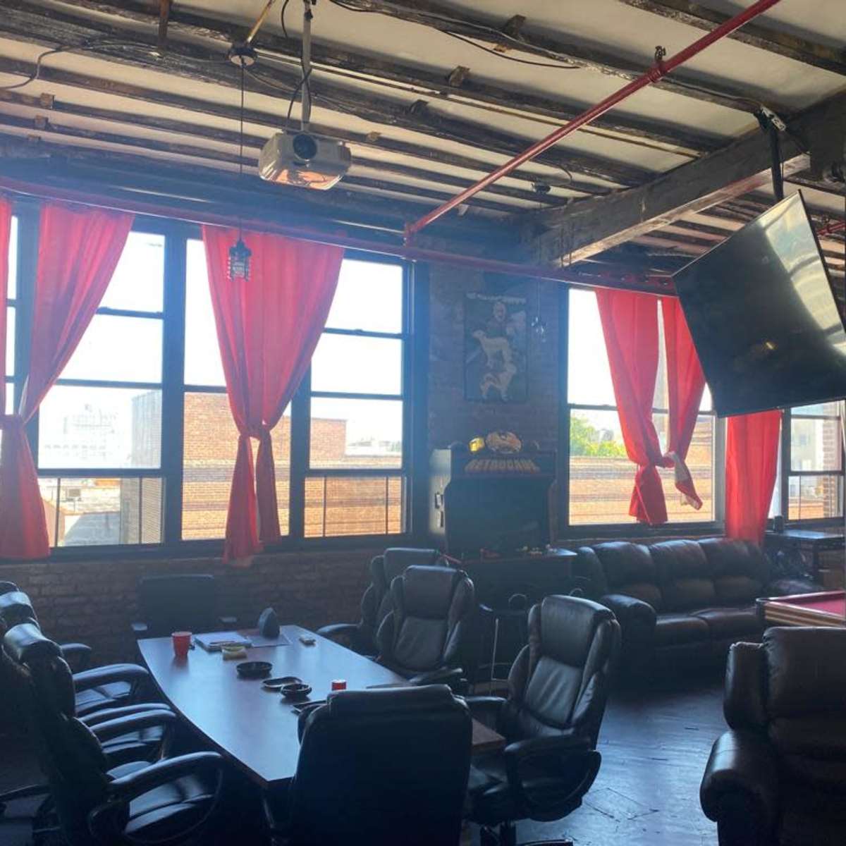 A spacious room with large windows, red curtains, a conference table surrounded by leather chairs, and a pool table in the corner.