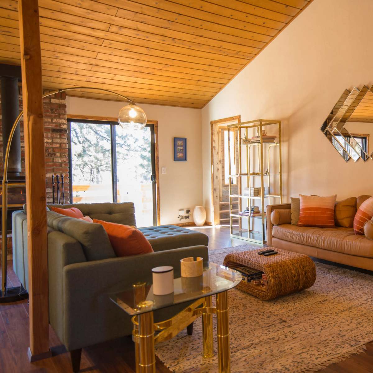 A cozy living room with two sofas, a coffee table, and a decorative mirror on the wall, surrounded by large windows that let in natural light.