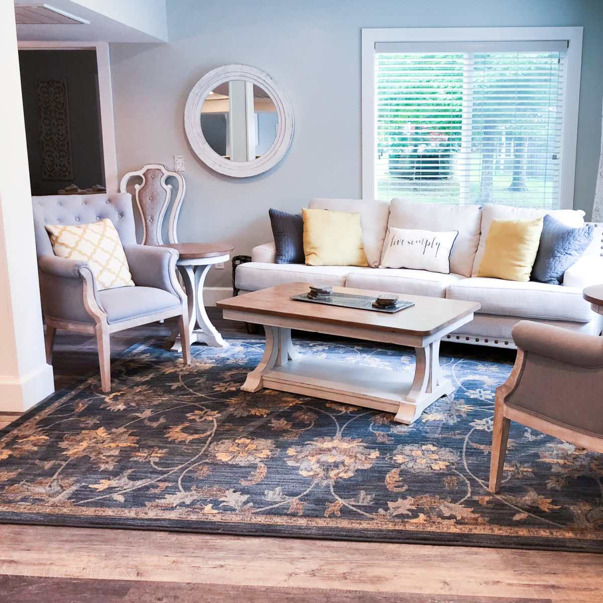 A living room with a gray sofa, two matching chairs, a coffee table, and a large area rug, all arranged around a window with natural light.
