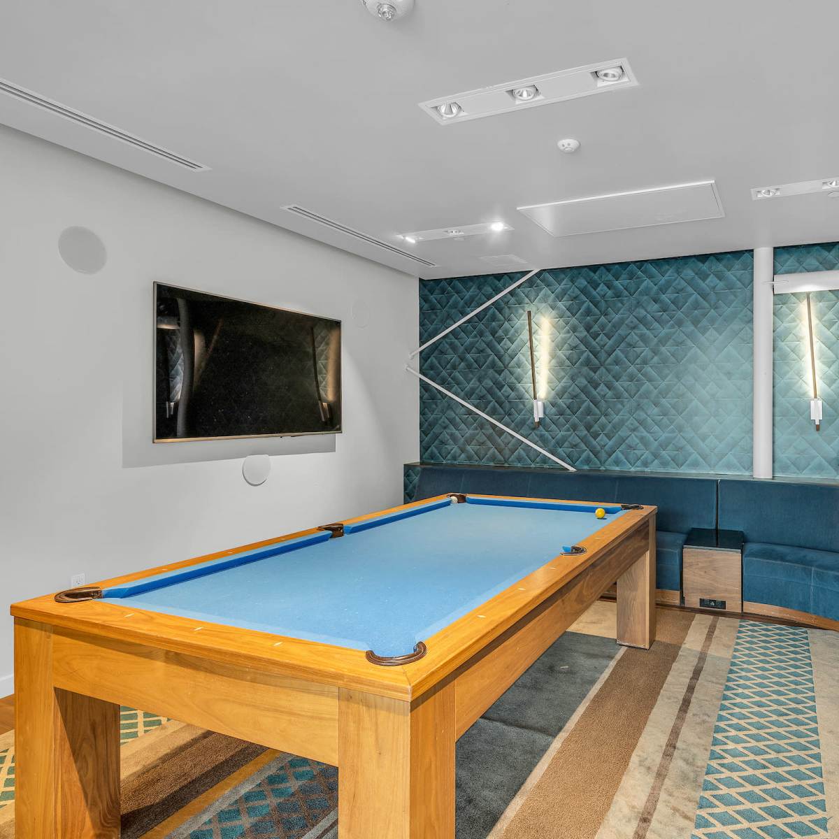A room features a blue felt pool table surrounded by a curved seating area and decorated with patterned wall panels.