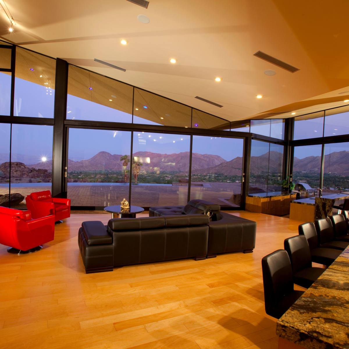 A modern living room features large windows with mountain views, sleek furniture, and a spacious layout.