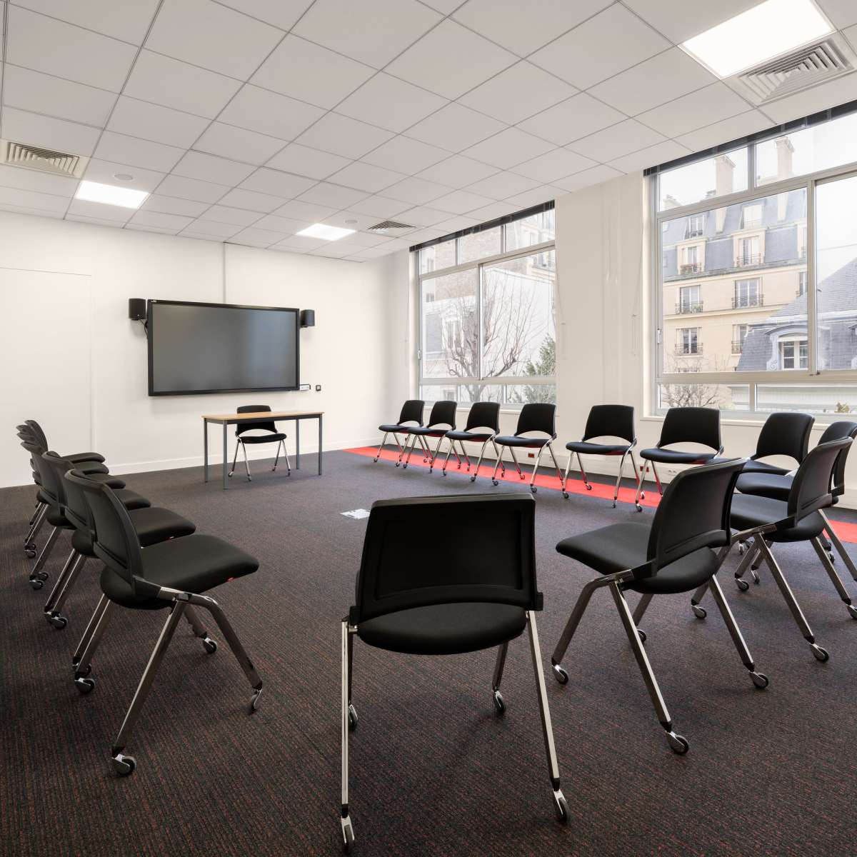 A meeting room is set up with chairs arranged in a circle facing a wall-mounted screen.