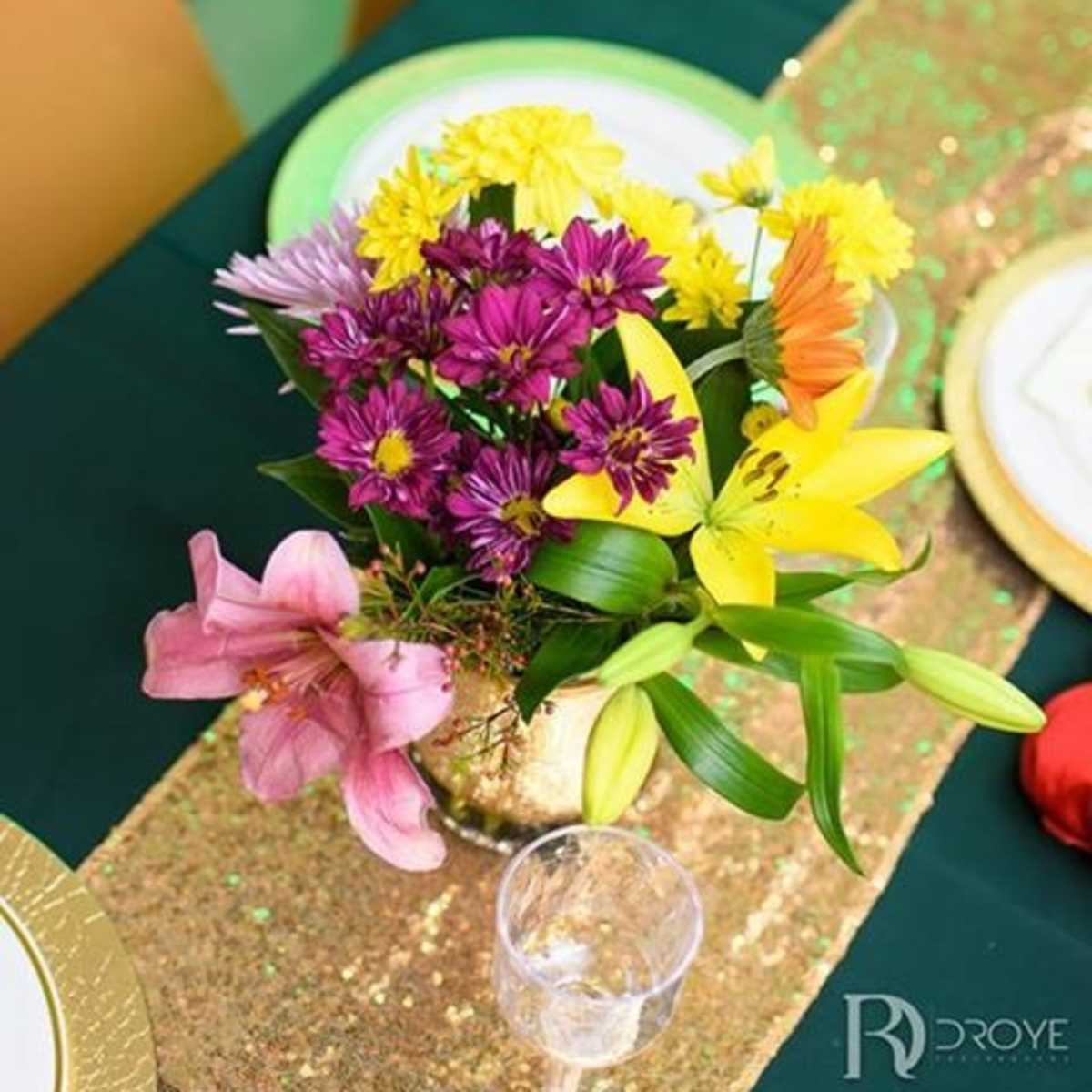 A centerpiece of multicolored flowers is placed on a dining table adorned with green and gold decorations.