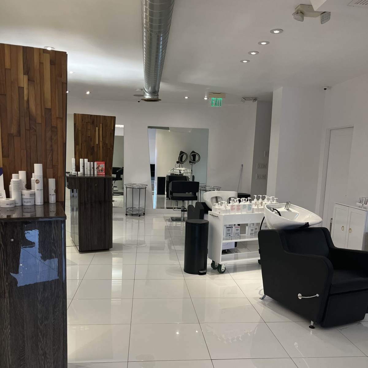 A modern salon interior featuring sleek white tiles, a wooden accent wall, a black seating area, and a styling station with mirrors and salon equipment.