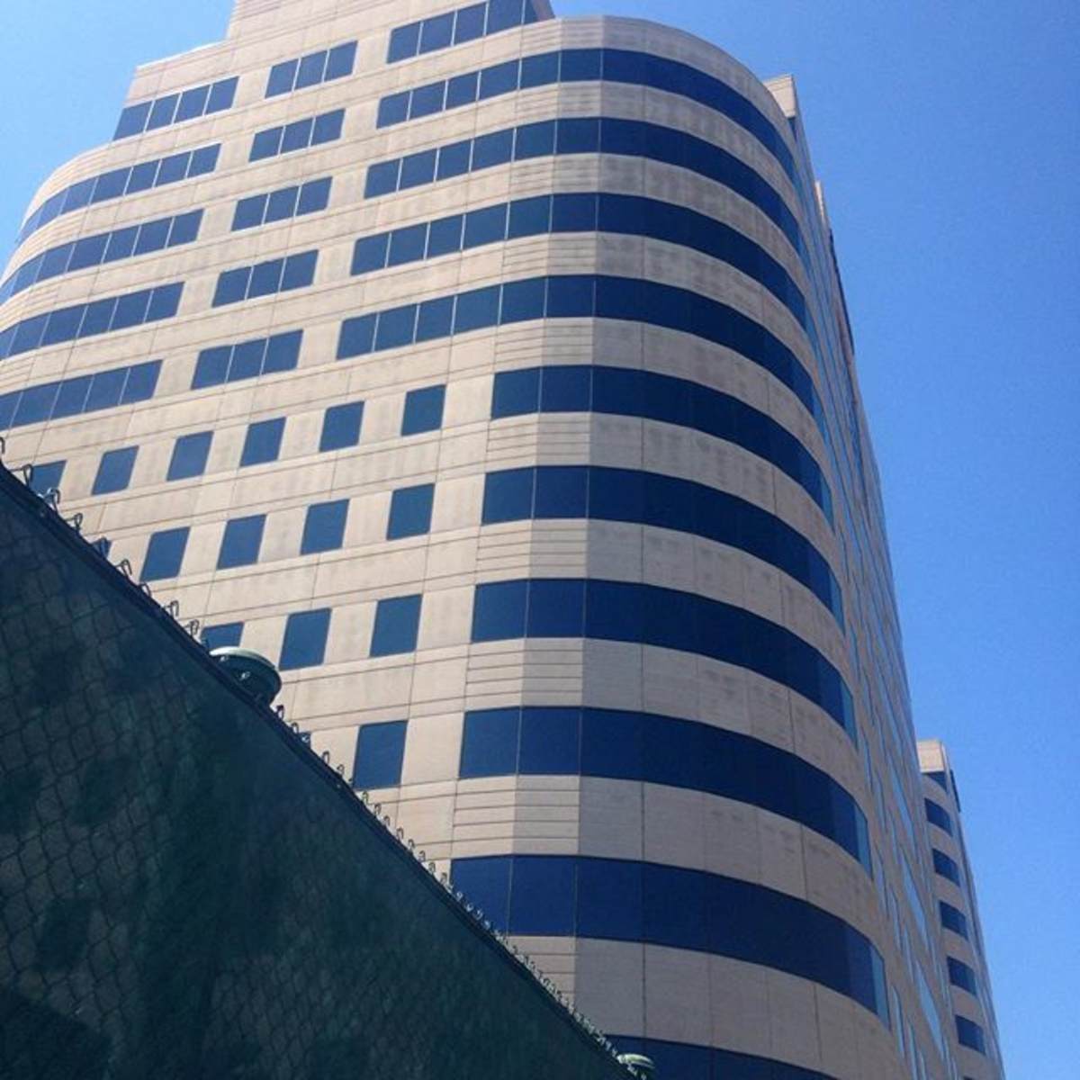 A modern office building with a curved facade and large blue windows stands against a clear blue sky.