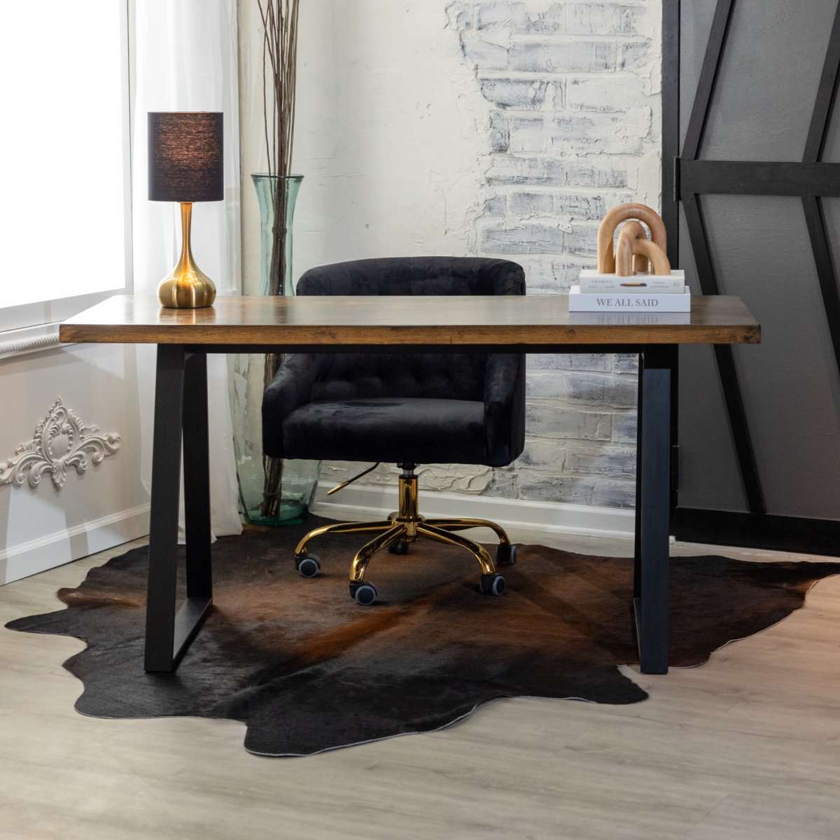 A modern workspace featuring a wooden desk with a black chair on wheels, a lamp, and decorative elements against a textured wall.