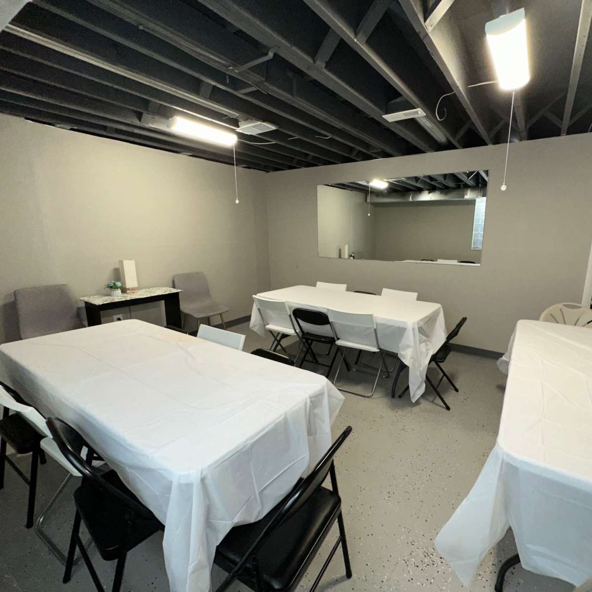 A basement room with several tables covered in white tablecloths, arranged in a seating area.