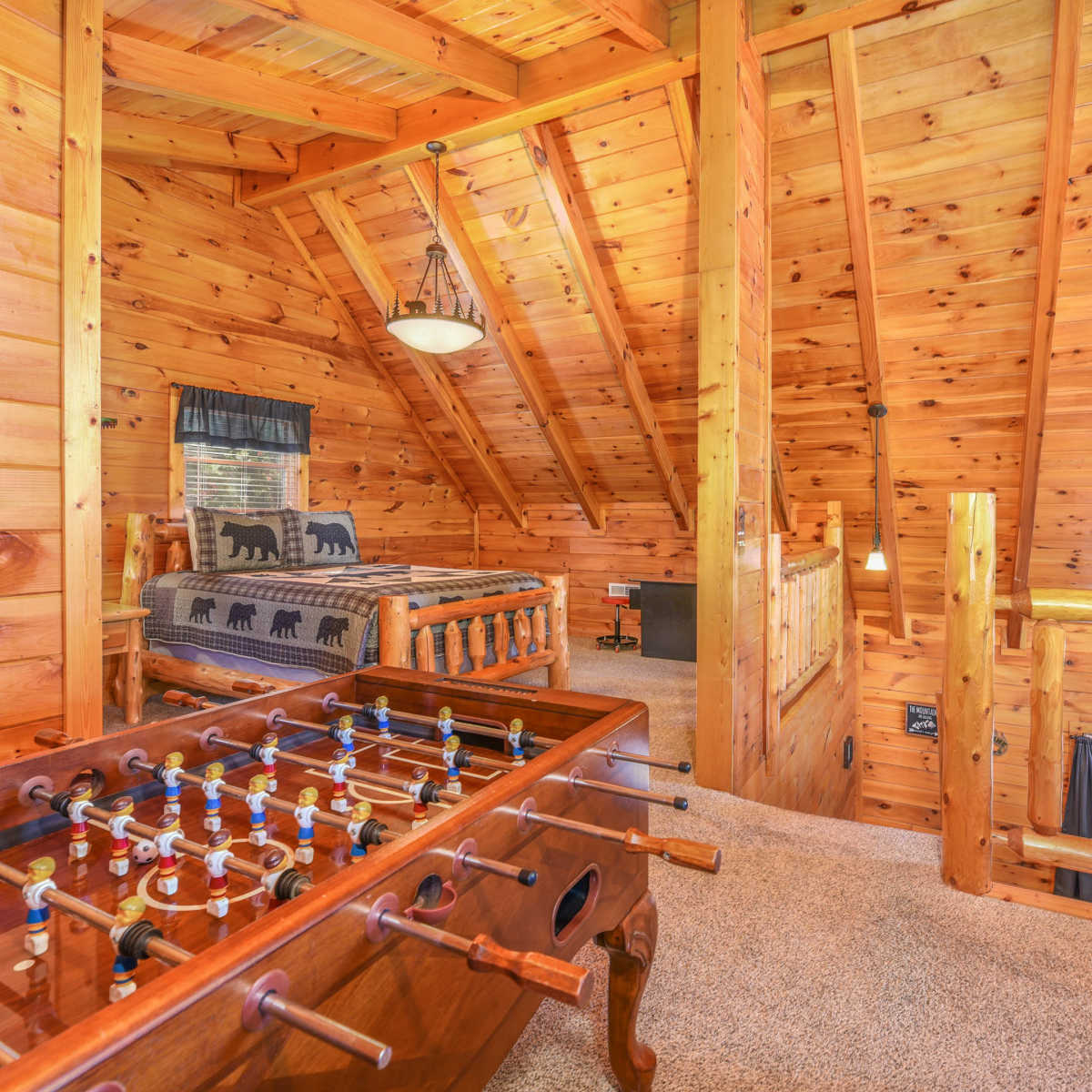 A loft area features a foosball table, a wooden bed, and a rustic pine wood ceiling.