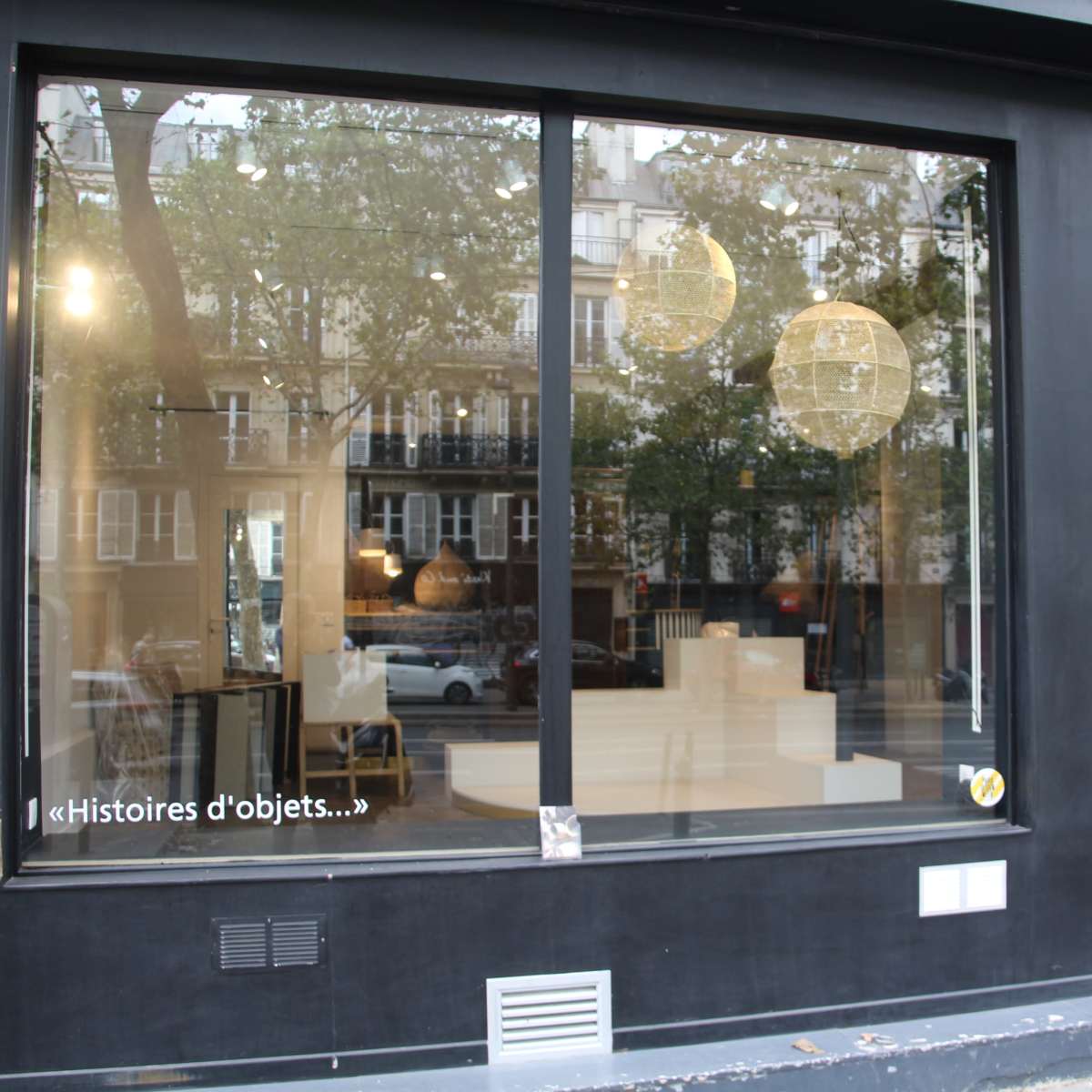 A storefront with large windows displaying minimalist interior decor and two pendant light fixtures.