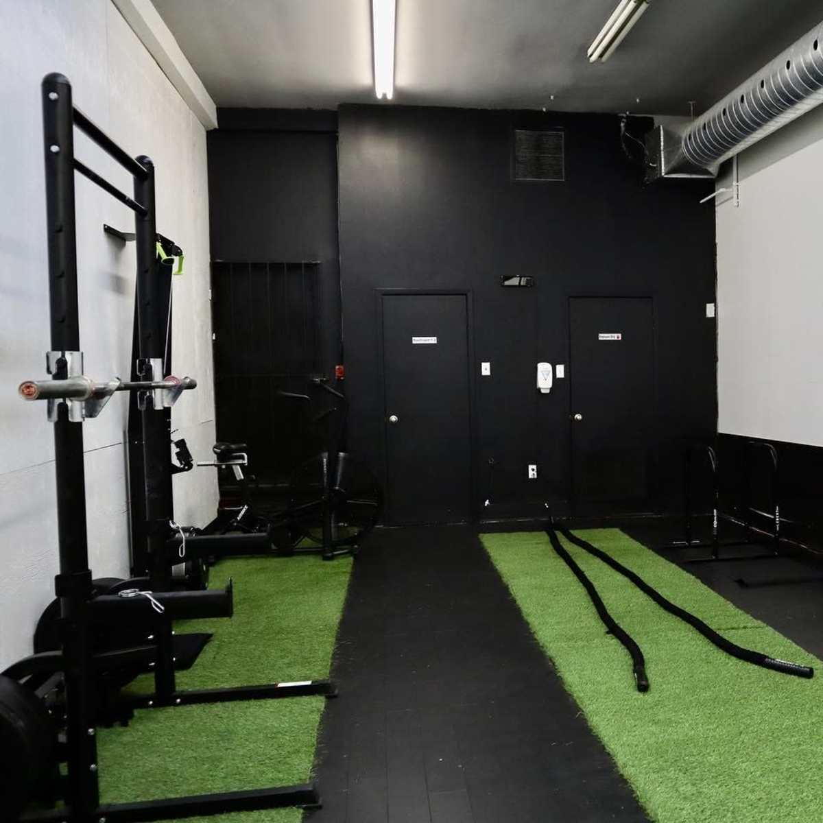 A minimalist gym space featuring exercise equipment, black walls, and artificial turf on the floor.