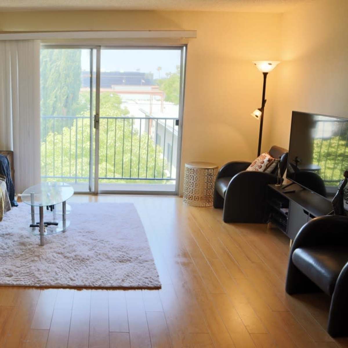 A bright living room features a couch, a glass coffee table, and a large window overlooking greenery.