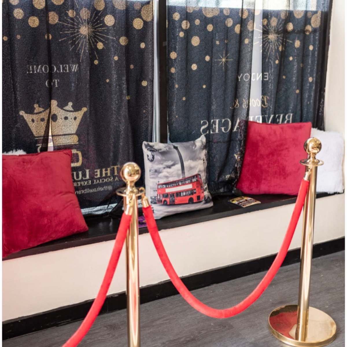 A seating area with decorative pillows and a red carpet barrier, framed by dark curtains featuring gold stars and crowns.