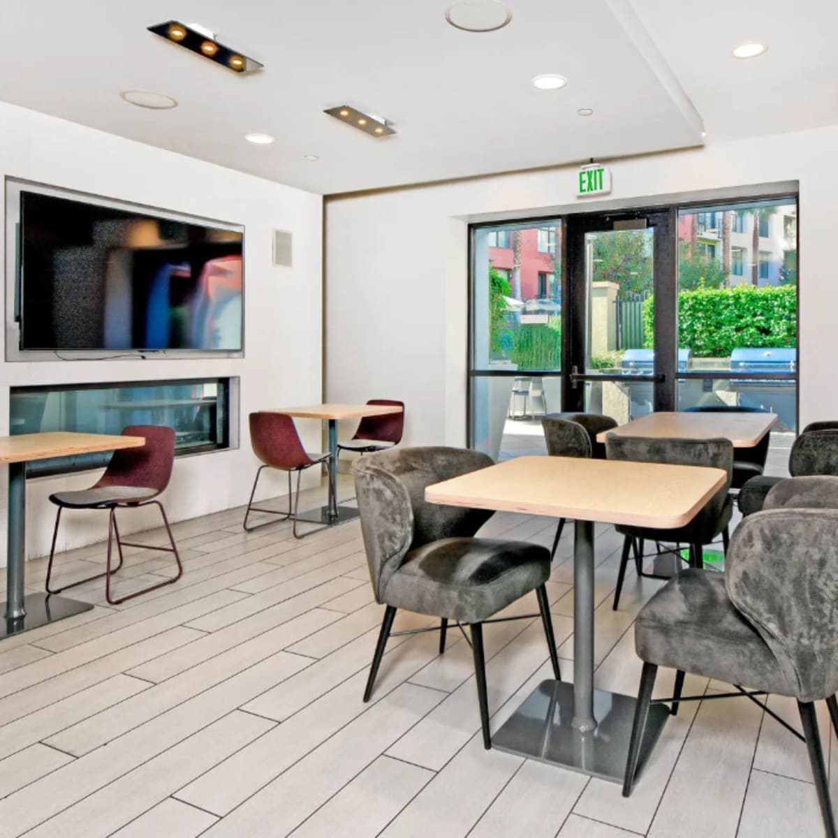 A modern interior space with several tables and chairs, a large wall-mounted television, and a glass door leading to an outdoor area.