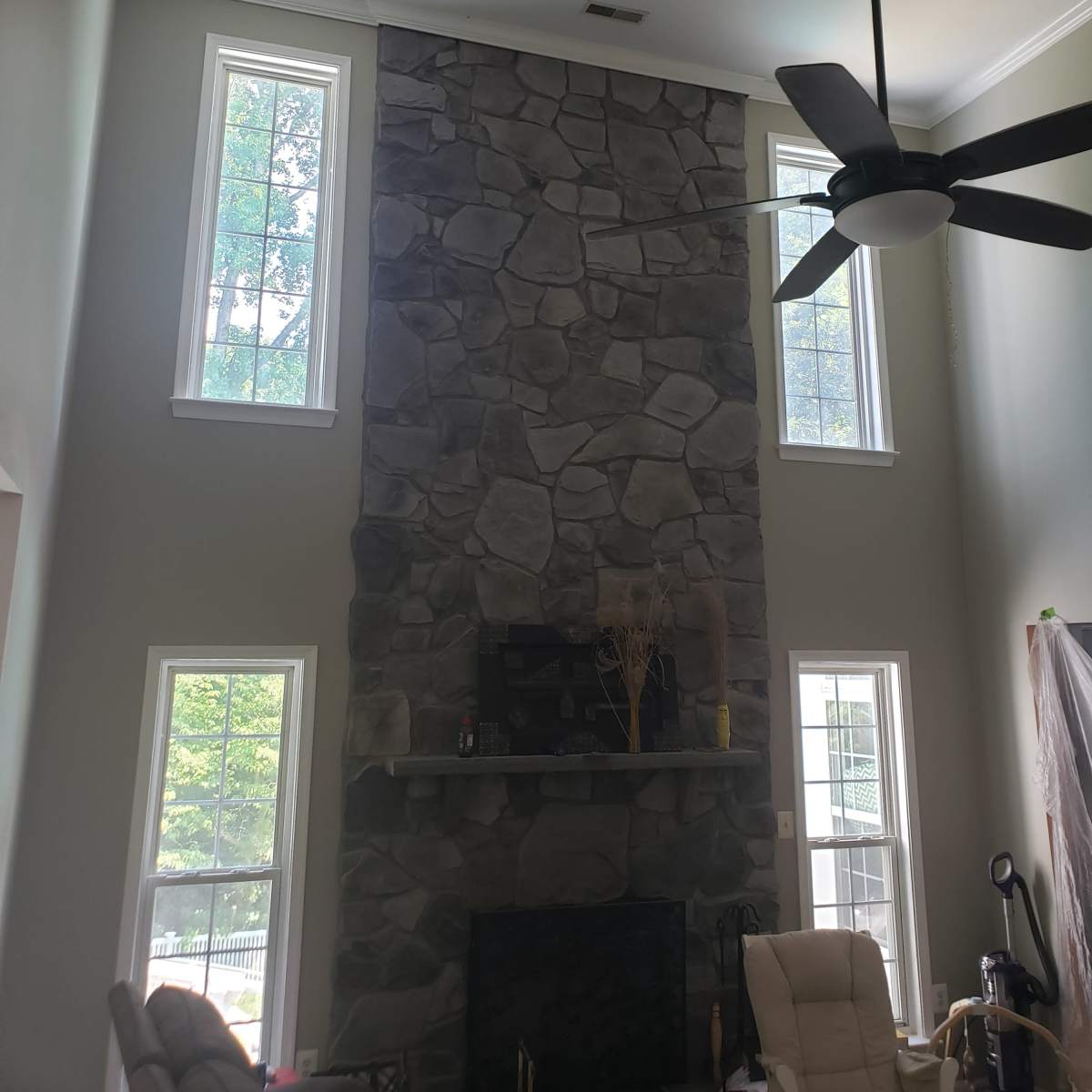 A spacious living room with a tall stone fireplace and large windows on either side.