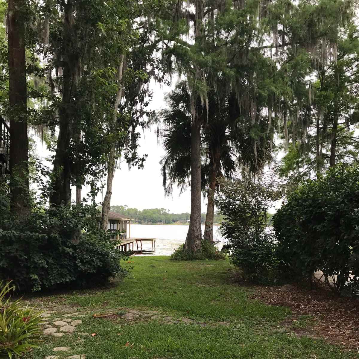 A path of stones leads through greenery to a lake surrounded by trees.