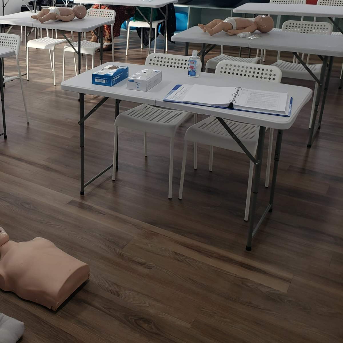 A classroom set up for CPR training with several mannequins on the floor and tables arranged around the room.