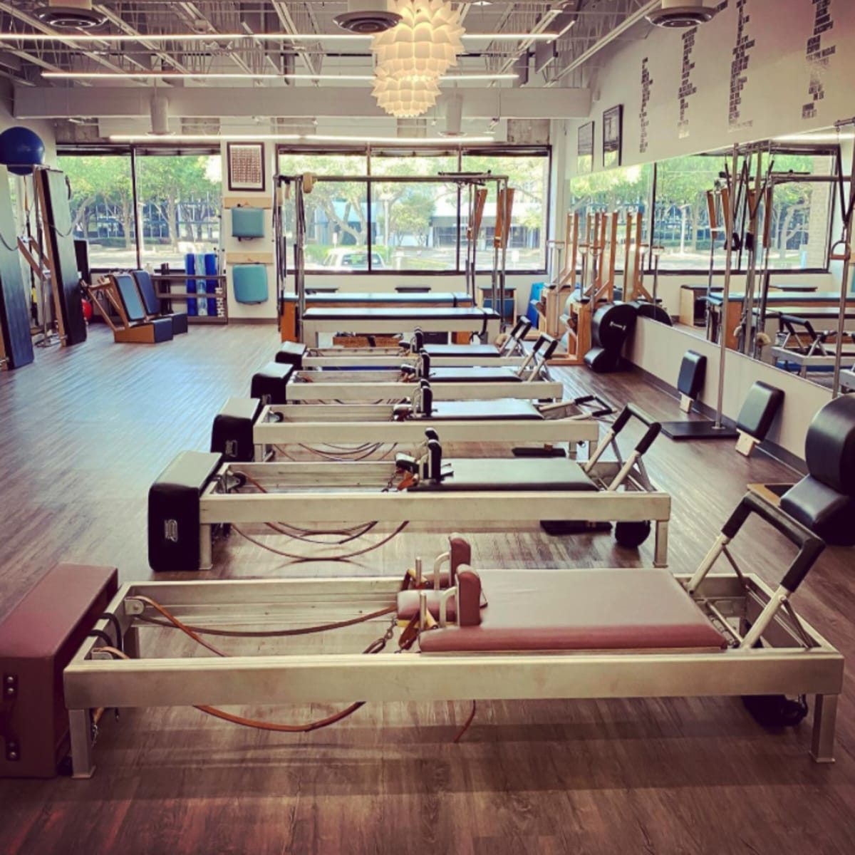 A bright, spacious pilates studio featuring several reformer machines arranged neatly along a wooden floor.