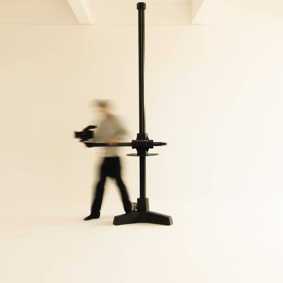 A person walks past a tall, black studio stand in a minimalistic, white room.