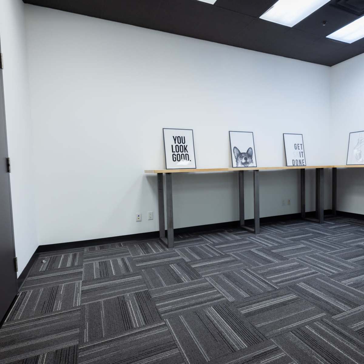 A minimalistic room with gray carpet, white walls, and several framed prints displayed on tables against one wall.