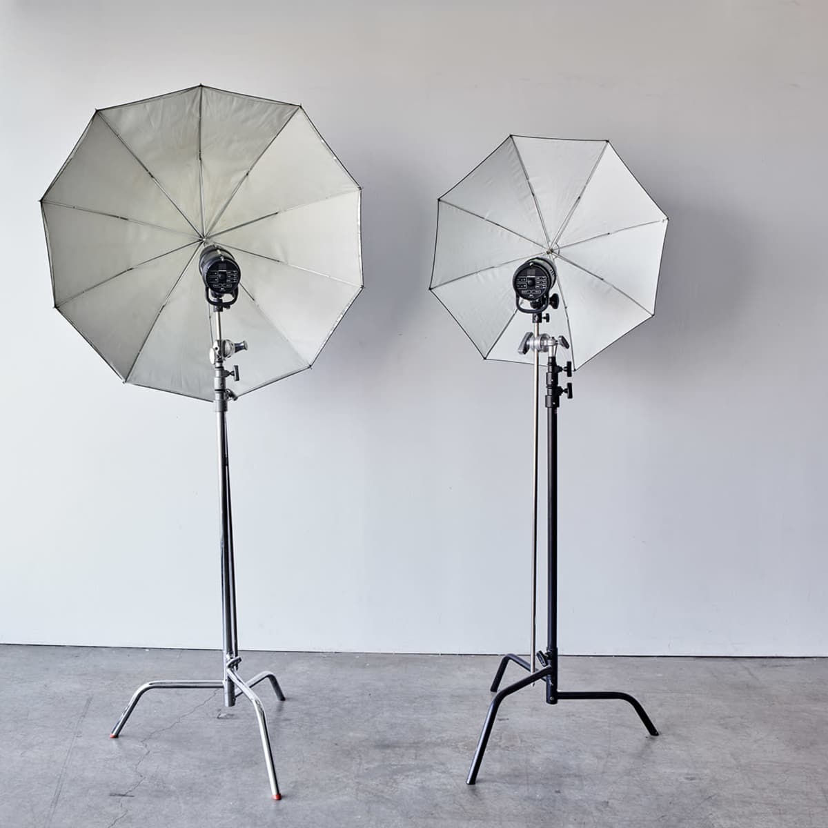 Two umbrella light softboxes are set up on stands in front of a plain white wall.