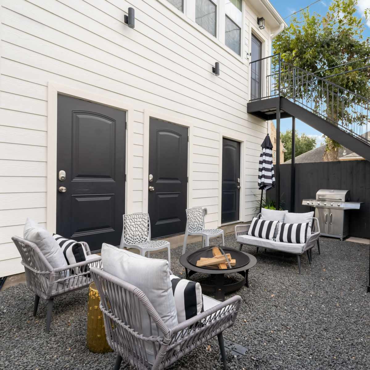 A residential outdoor area with a seating arrangement, a small table, a barbecue grill, and stairs leading to an upper level.