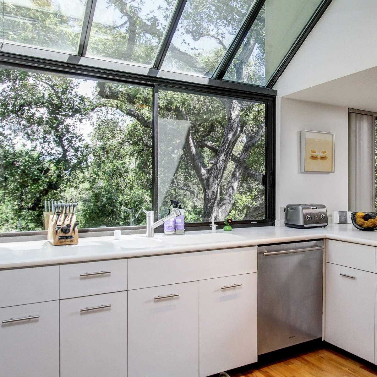 A modern kitchen featuring a central island, stainless steel appliances, and large windows overlooking greenery.