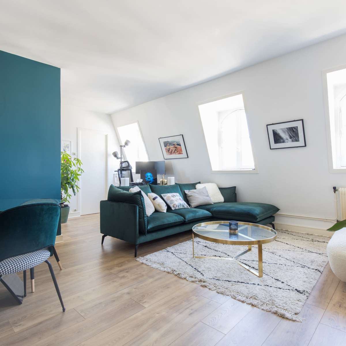 A modern living room features a green accent wall, a comfortable sofa, a glass coffee table, and large windows that allow natural light to fill the space.