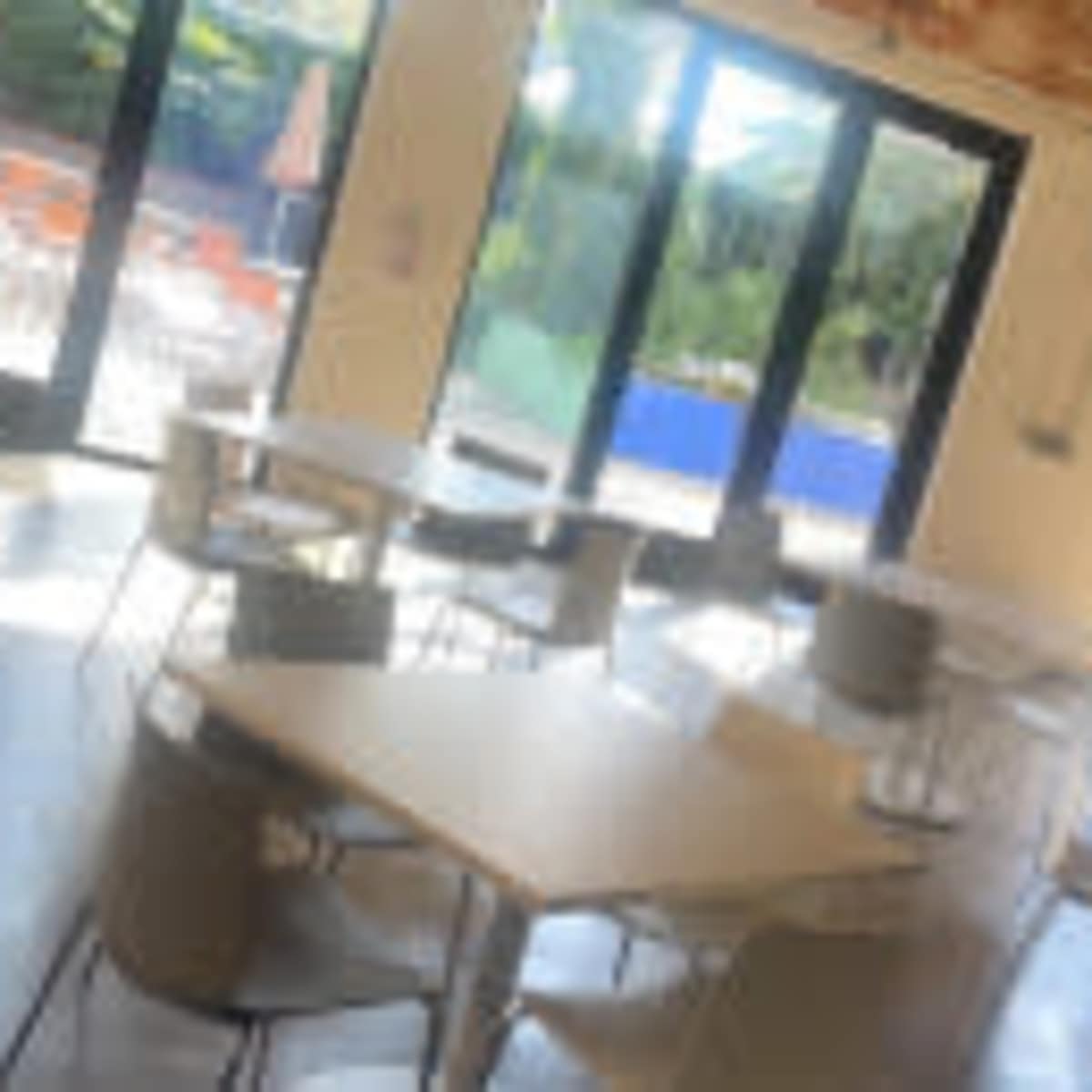 A bright, modern dining area with several tables and chairs, large windows, and a view of an outdoor space.
