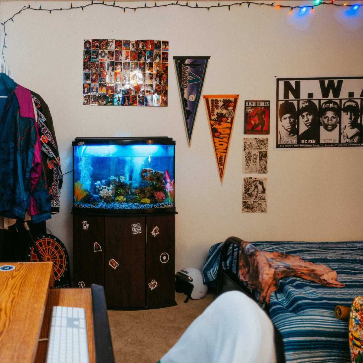 A colorful room featuring a computer desk, an aquarium, and a bed with a striped blanket, along with various posters and decorations on the walls.