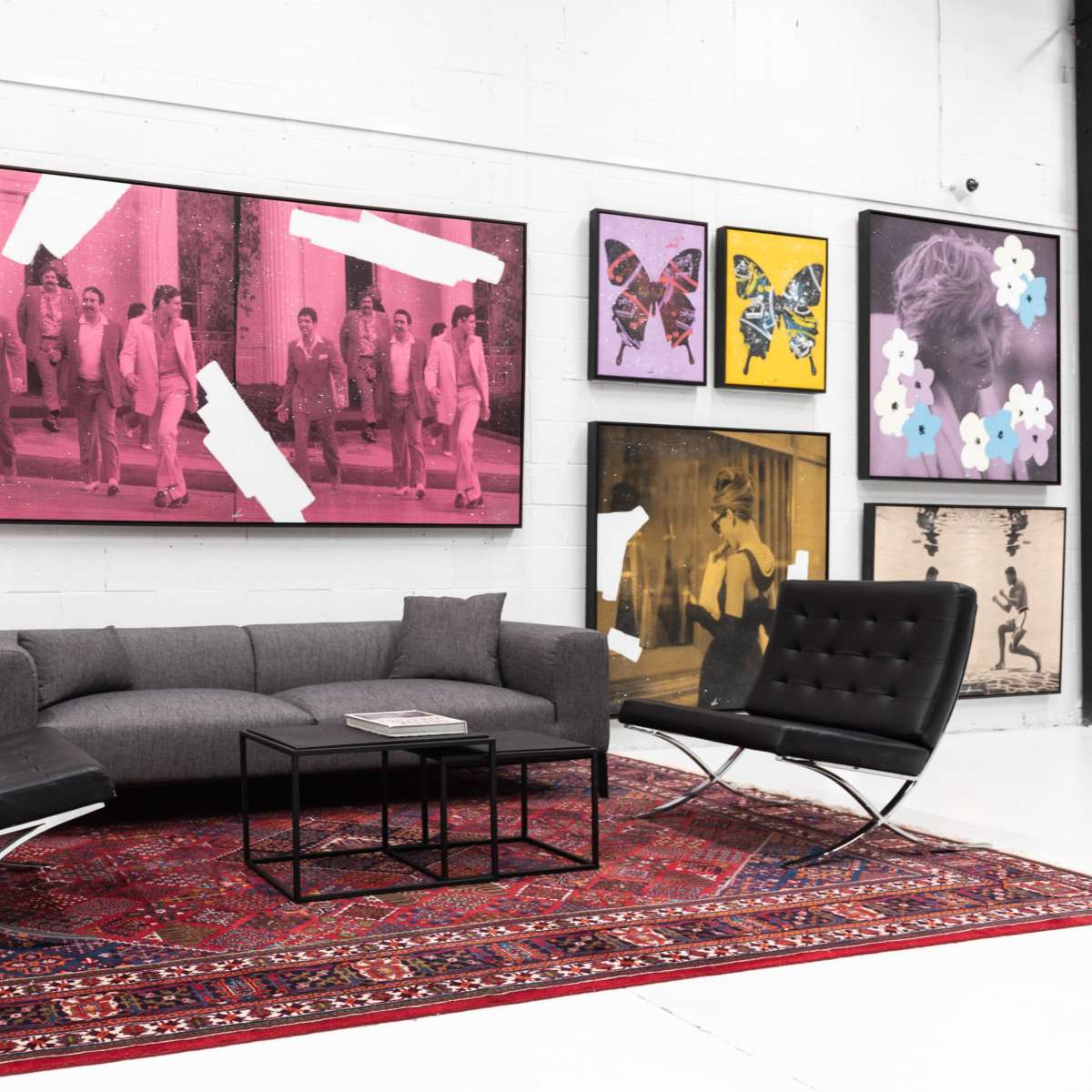 A modern living space featuring a gray sofa, two black chairs, a coffee table, and an array of framed art on the walls.