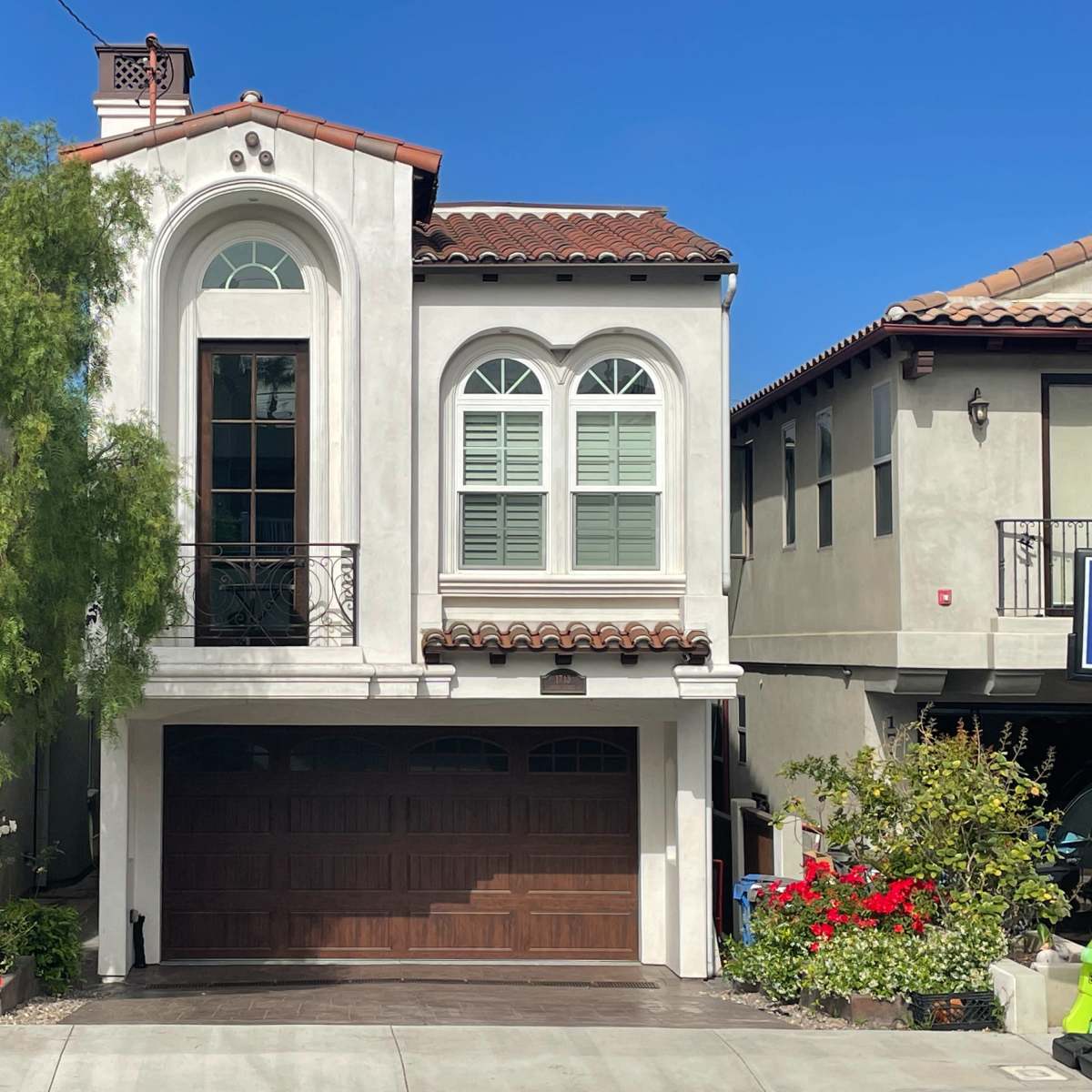 A two-story residential house with arched windows, a wooden garage door, and a landscaped front yard.