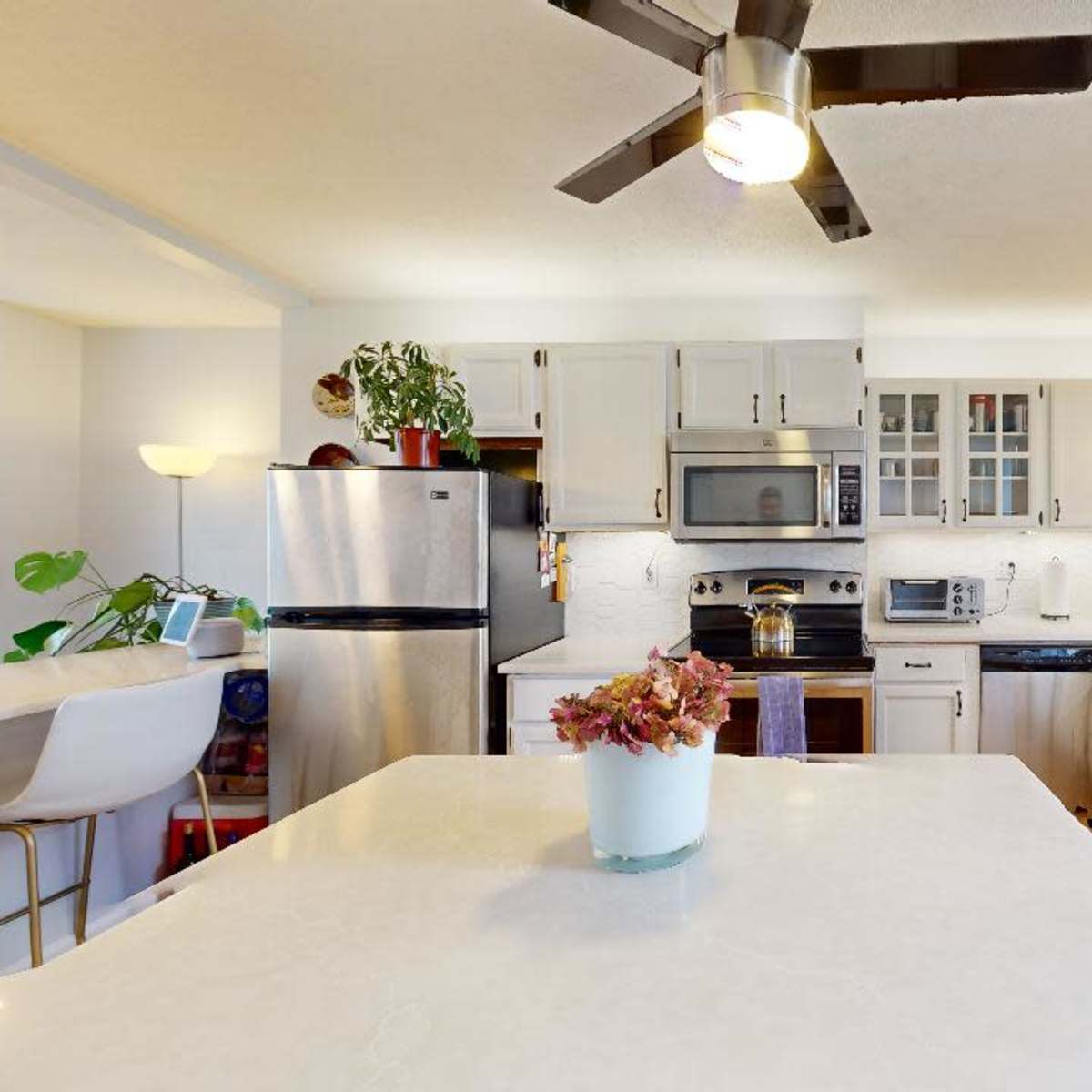 A modern kitchen features white cabinetry, stainless steel appliances, and a central island with a white countertop.