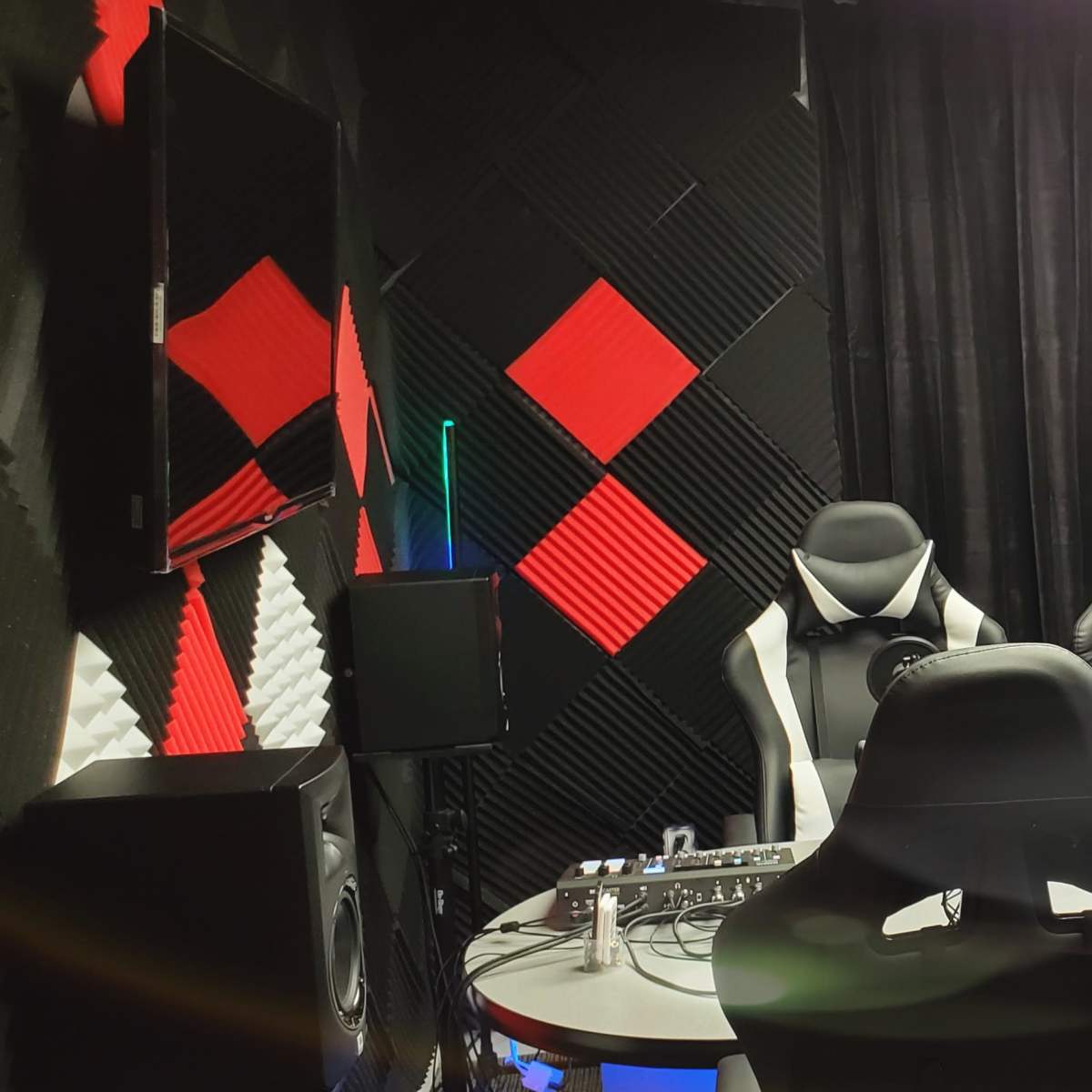 A soundproof room designed for recording, featuring three chairs with microphones and a table surrounded by black and red acoustic panels.