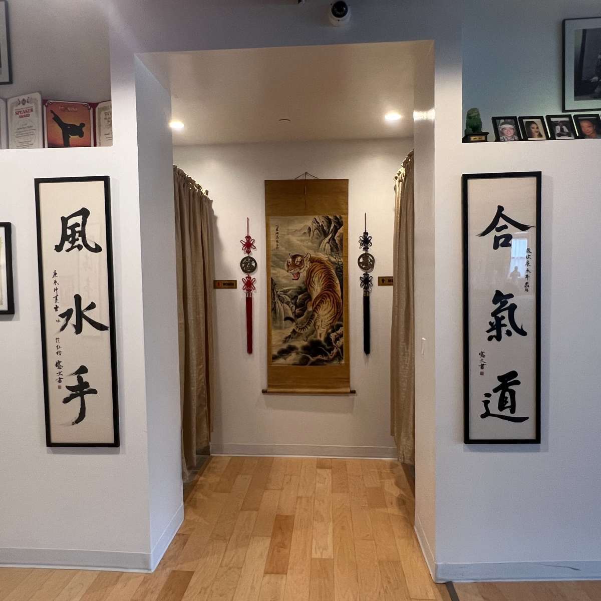 A hallway with framed certificates and photographs on the walls, flanked by curtains leading to a decorated space featuring a tiger-themed artwork.
