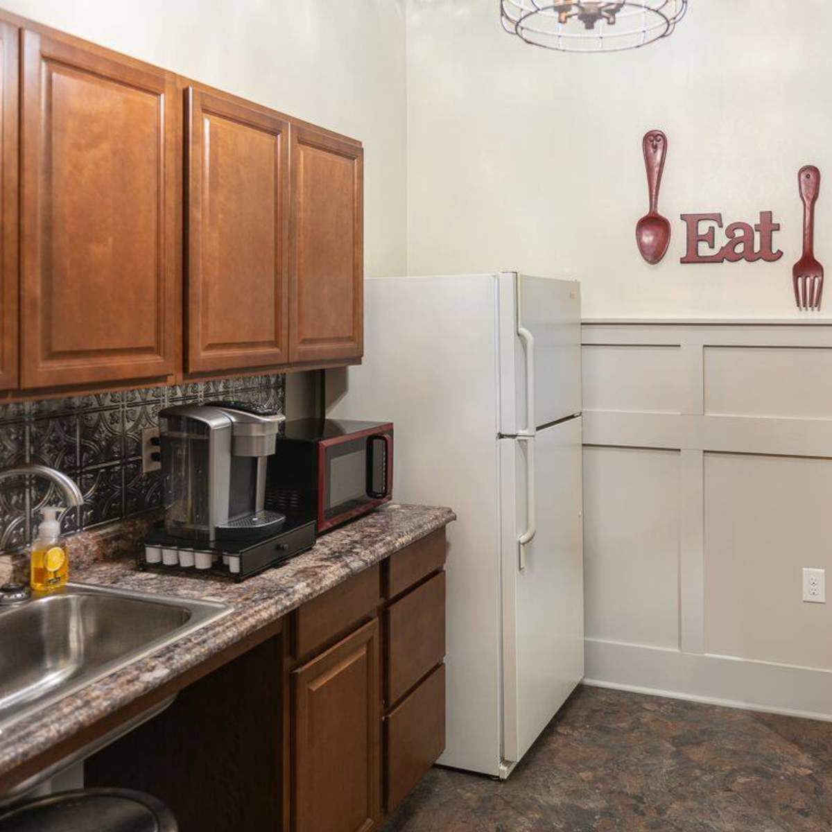 A compact kitchen with wooden cabinets, a stainless steel sink, a white refrigerator, and a coffee maker on the counter.