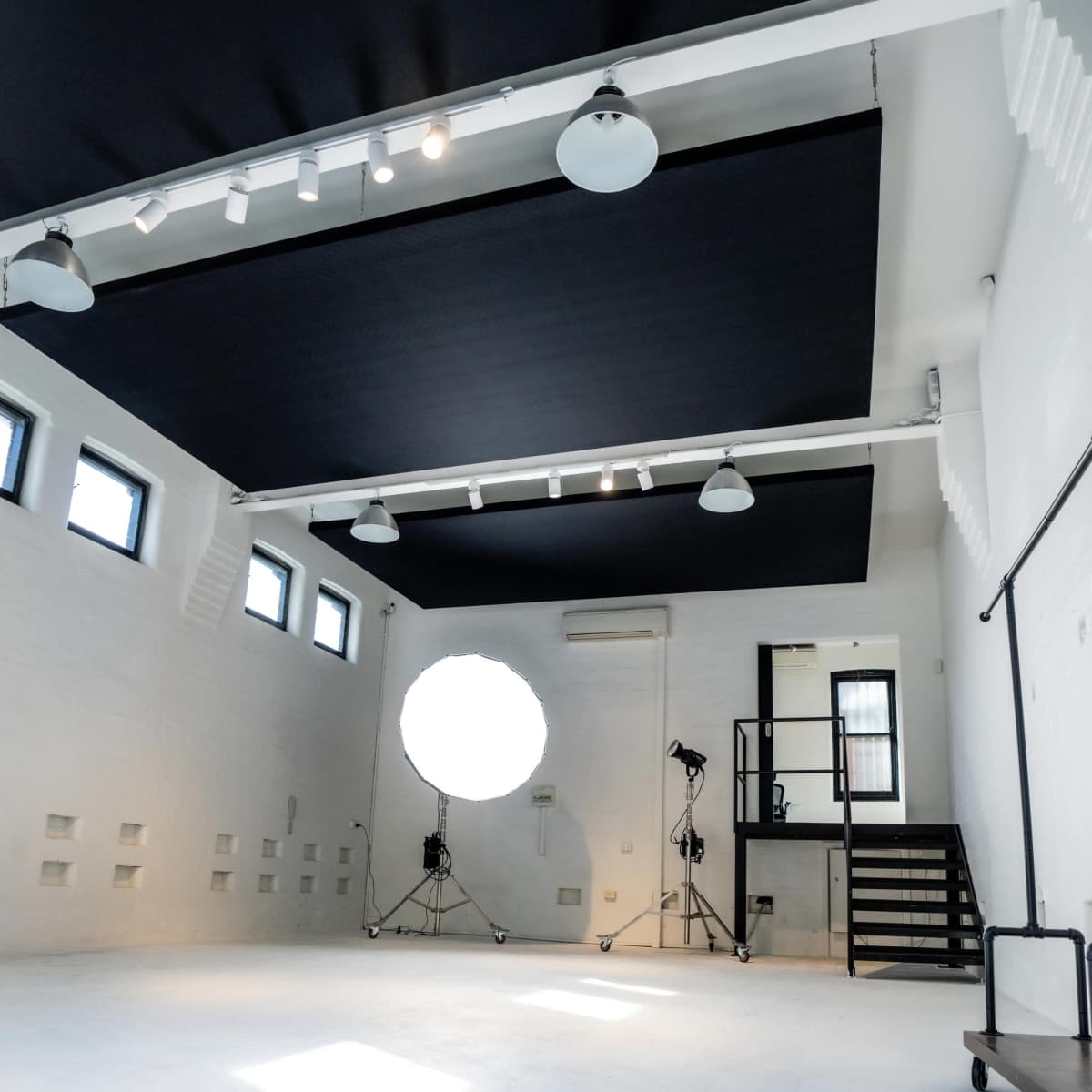 A spacious photography studio with a white floor, black overhead panels, and a large circular softbox on a stand.