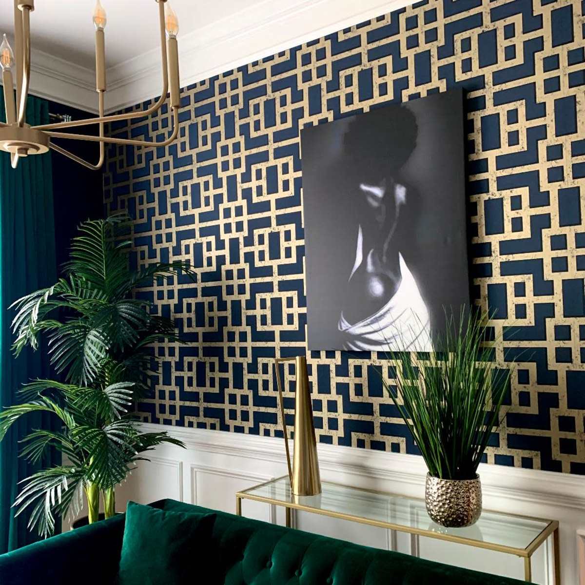 A stylish living room with a dark patterned wall, a large black and white artwork, a green velvet sofa, and decorative plants.