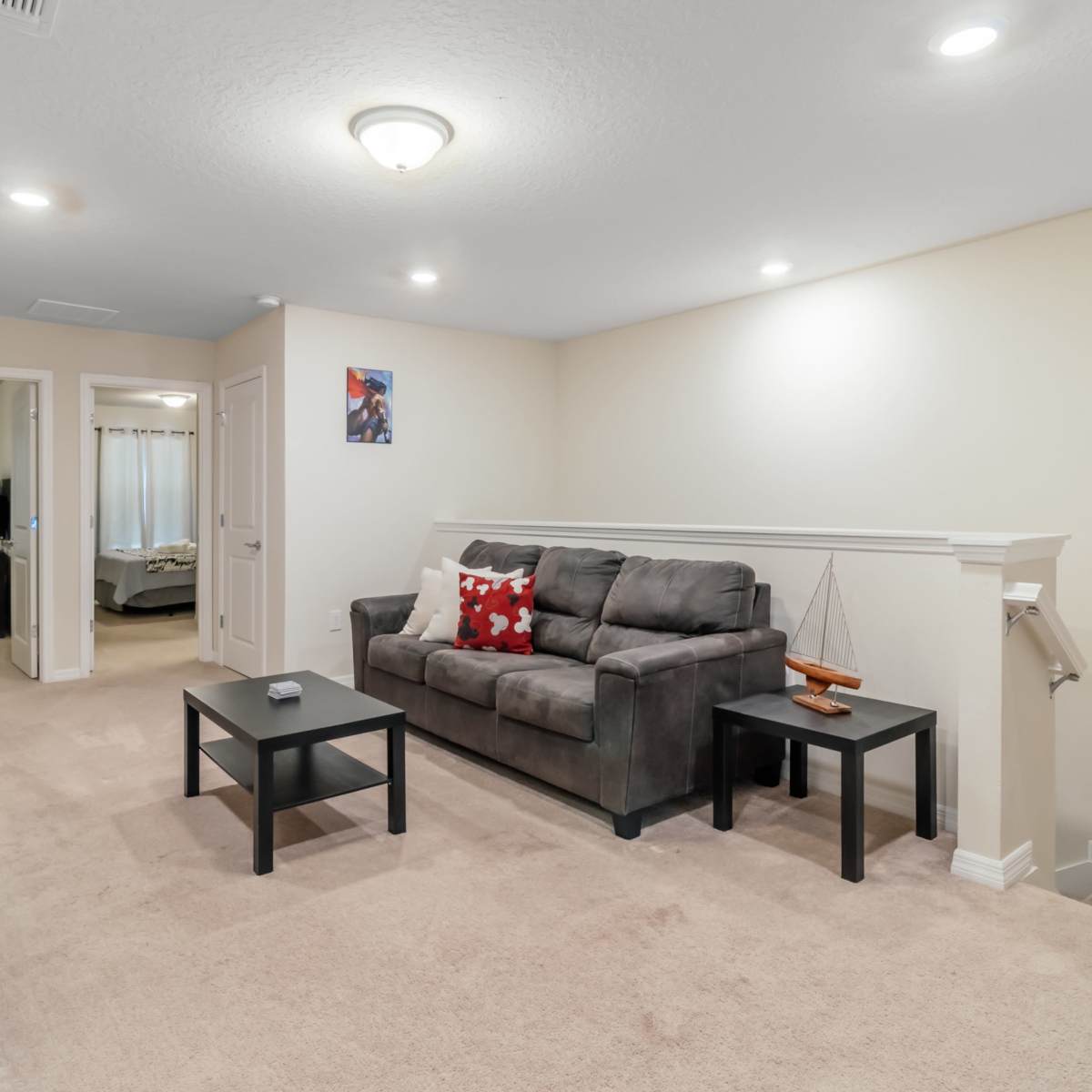 A cozy living area with a gray sofa and two black tables, set on beige carpet, leading to a doorway that connects to another room.