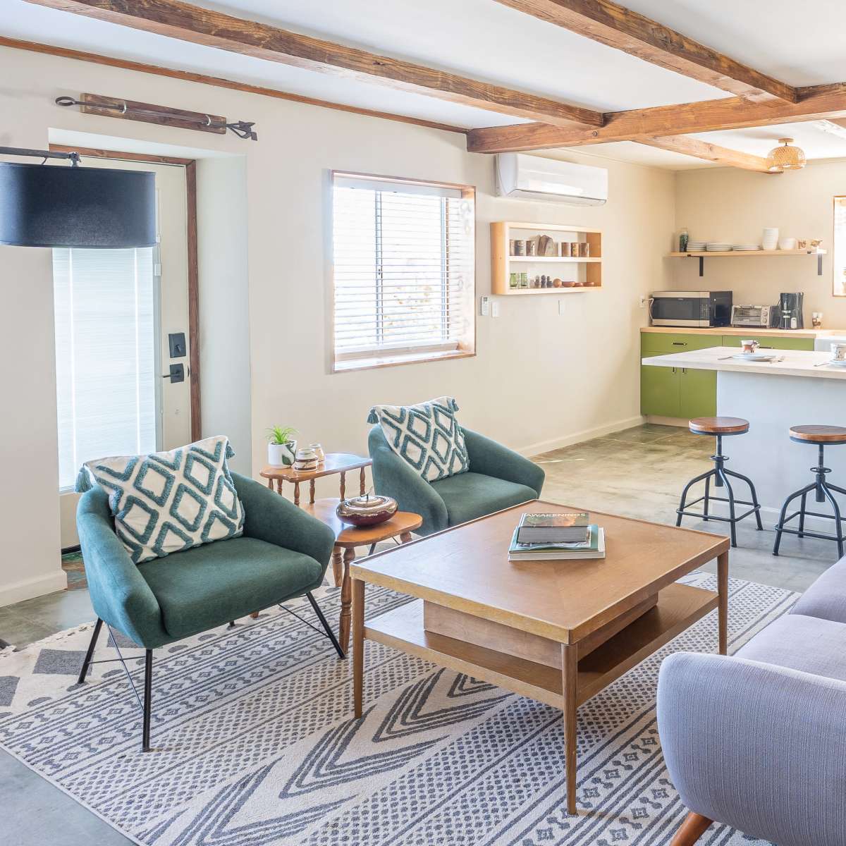 A cozy living room features a table surrounded by a sofa and two armchairs, with a kitchen area visible in the background.