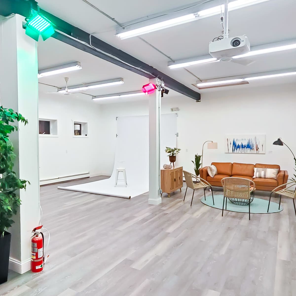 A modern, brightly lit studio space featuring a brown sofa, a circular coffee table, and a small white backdrop area.